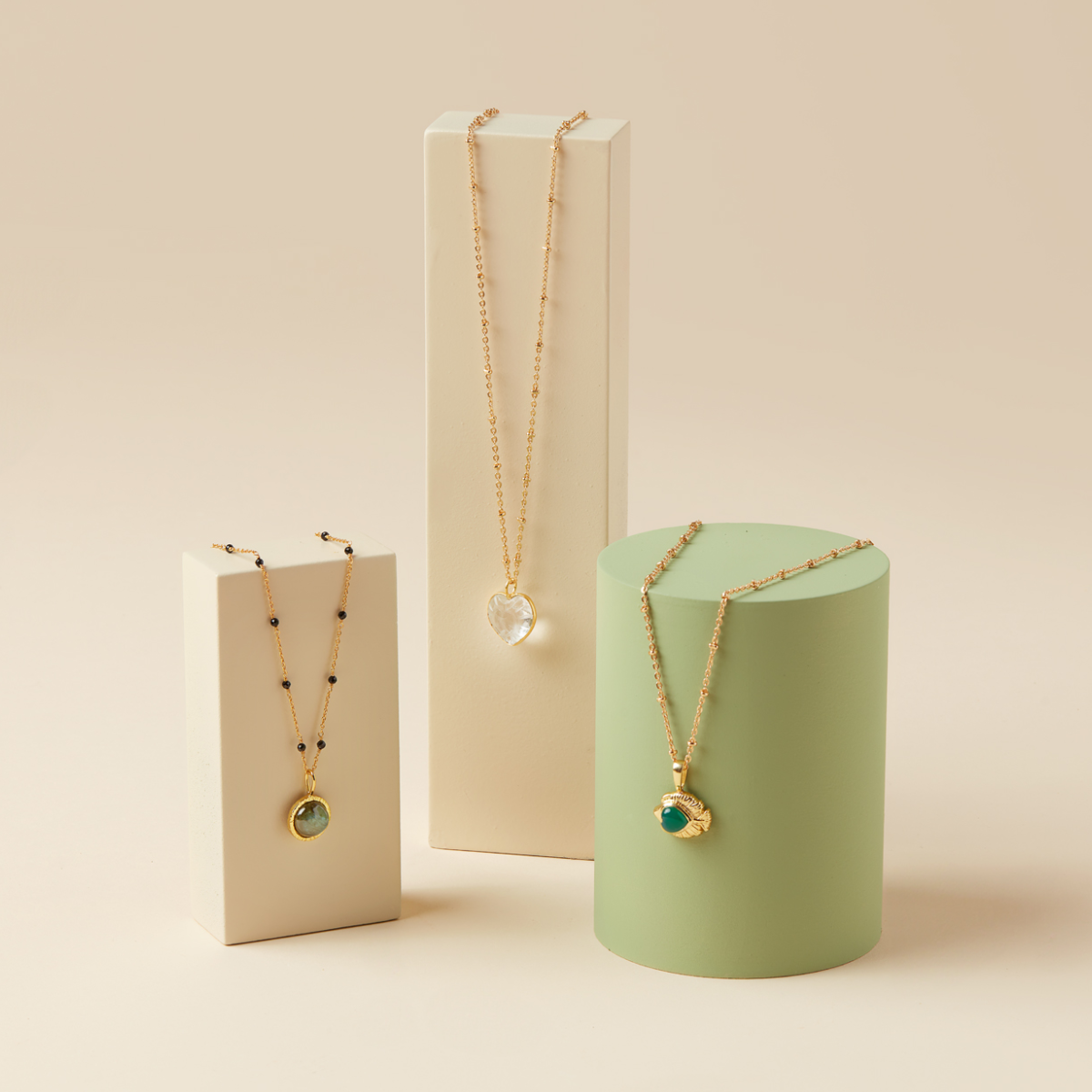 Three understated gold chain necklaces with pendants of carved rock crystal, labradorite in a gold frame, and emerald in a fish-shaped charm